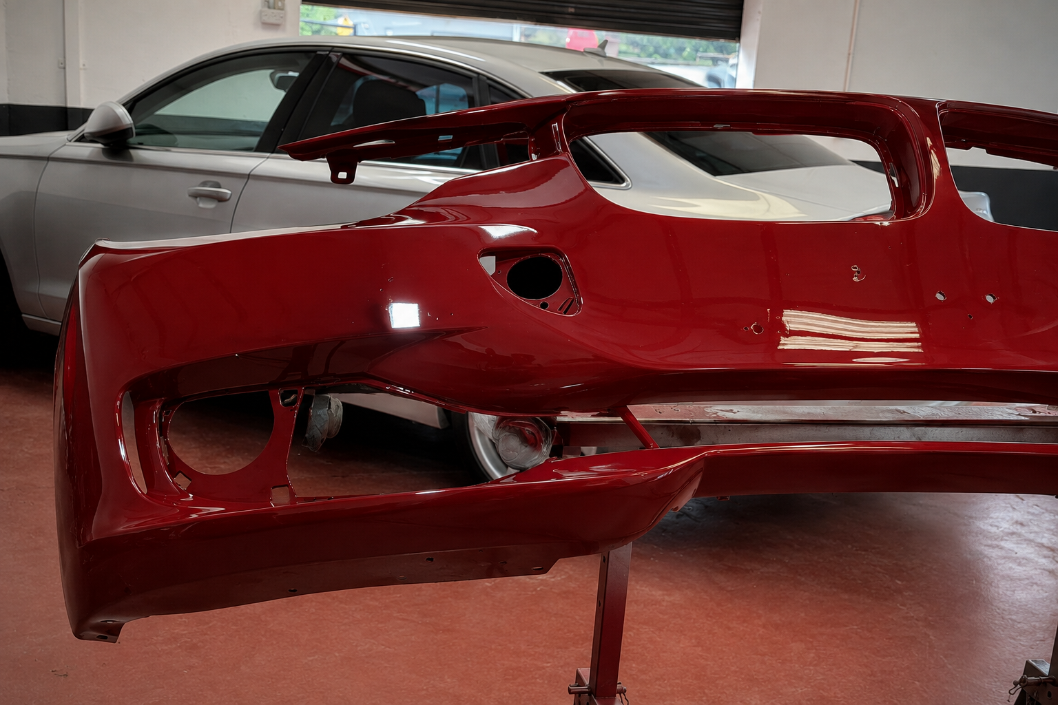 The refinished deep red Jaguar front bumper on a stand in the Portadown workshop, showing an even gloss finish across the whole panel