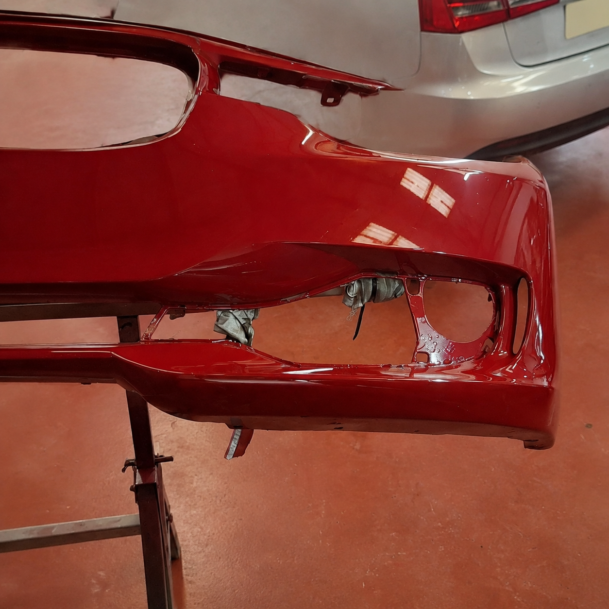 Close-up of the refinished Jaguar front bumper corner and fog light aperture, showing the depth and reflections of the finished red paint
