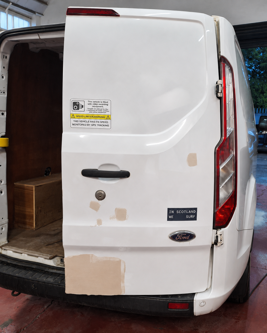 Close-up of the open right rear door of a white Ford Transit Custom during preparation, with several filler patches sanded flush around the lower door and handle