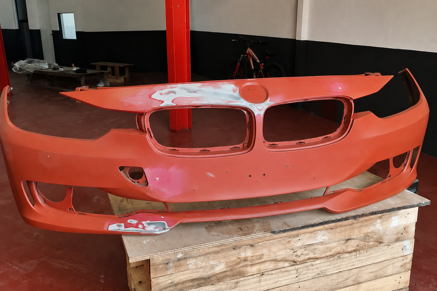 The detached Jaguar front bumper in primer during preparation, with filler applied and sanded areas visible around the grille openings